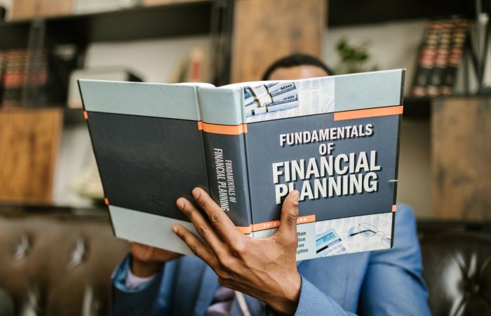 A professional individual in a suit reading 'Fundamentals of Financial Planning' indoors.