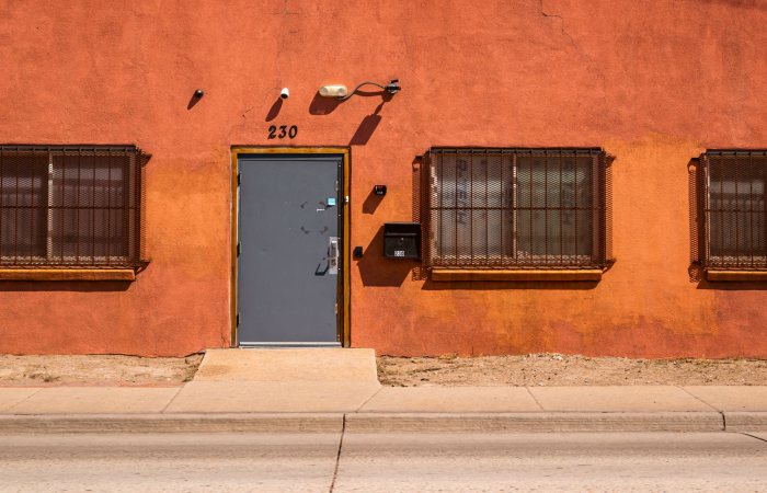An orange facade with a sturdy metal door and barred windows under bright daylight.