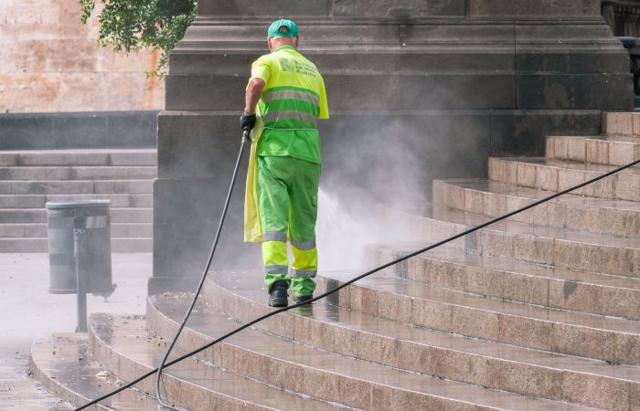 A municipal worker power washing stone steps outdoors, ensuring cleanliness and maintenance.