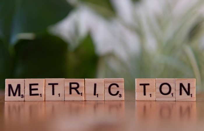 Scrabble tiles on a brown surface spell 'Metric Ton' with blurred green background.