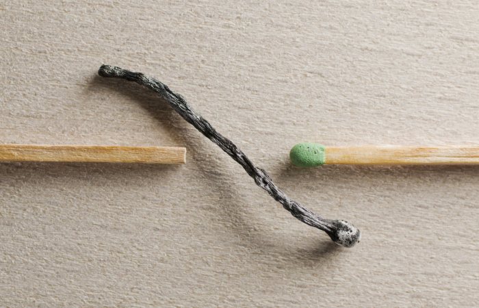 Artistic depiction of contrast between a burnt and unused match on a textured surface.