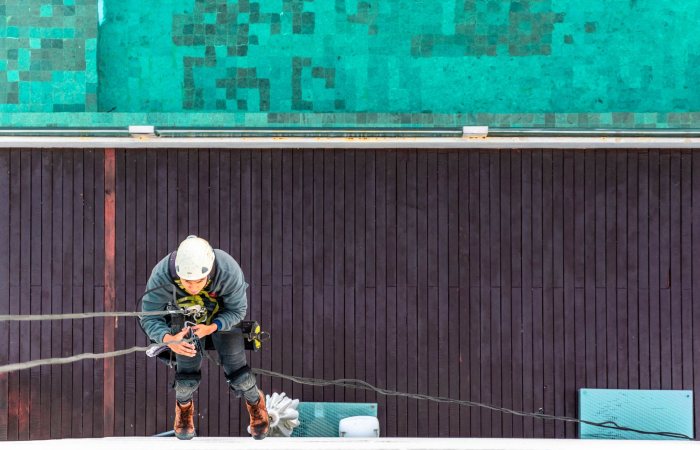 A worker using safety equipment for exterior building maintenance, viewed from above.