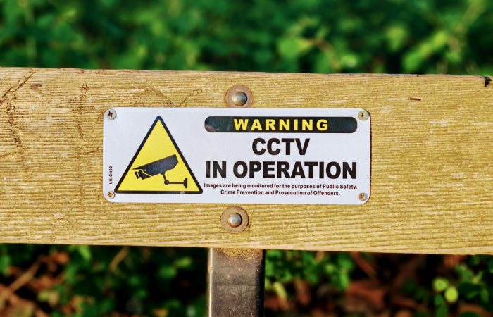 Wooden bench with a CCTV in operation warning sign, emphasizing public safety.