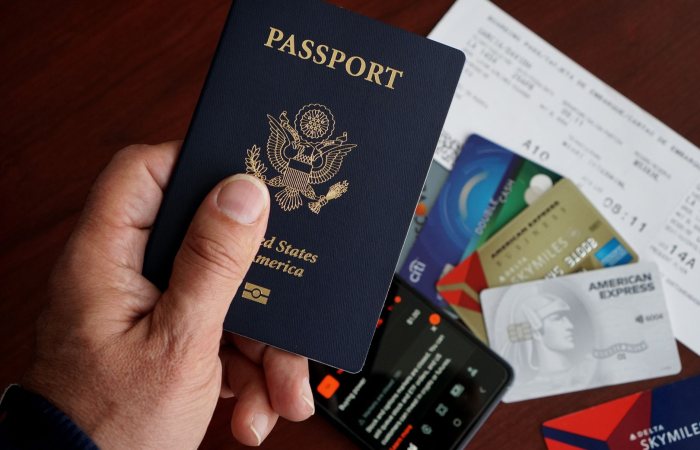 A close-up of a US passport with credit cards, tickets, and a mobile phone on a table.